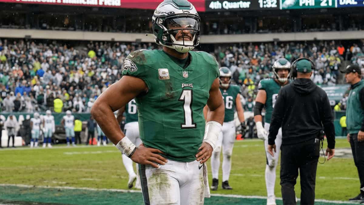 Jalen Hurts standing on the field in a Philadelphia Eagles uniform during an NFL game, looking focused on the sideline.