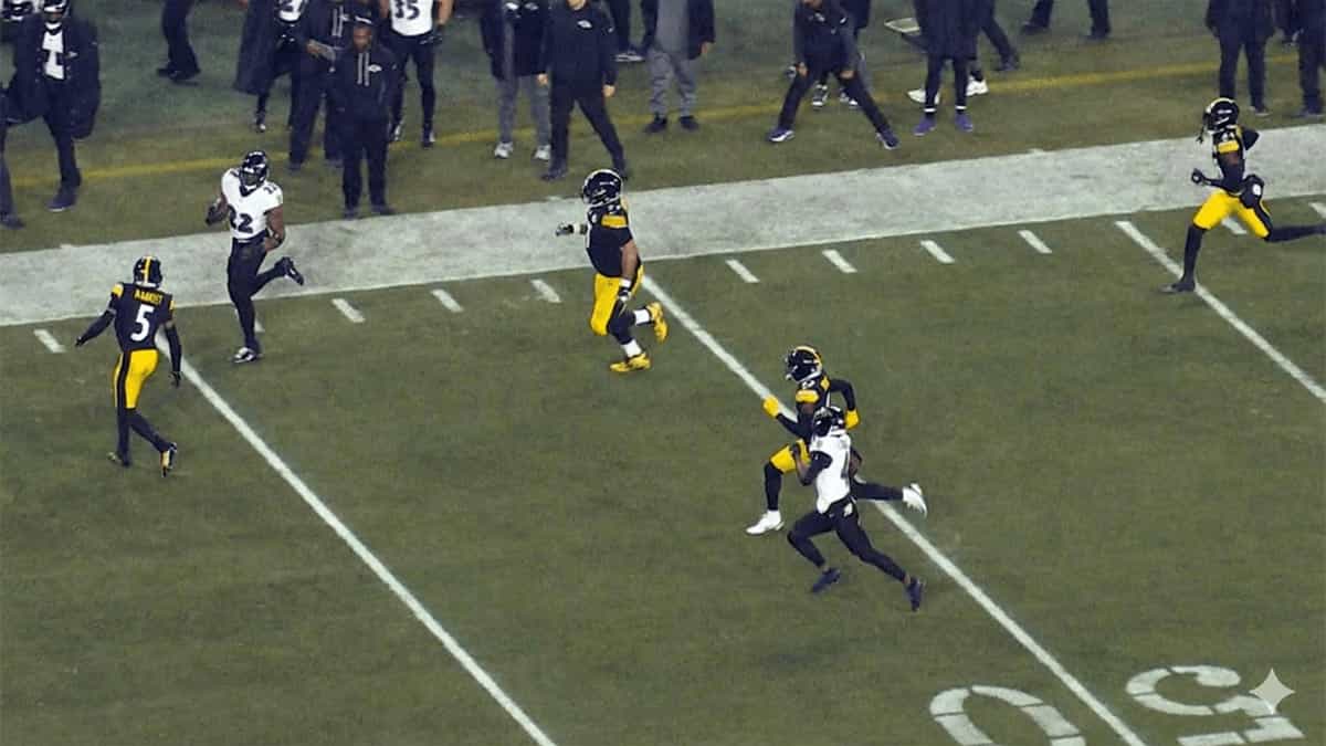 Ravens ball carrier runs along the sideline while Steelers defenders chase during an NFL rivalry game.